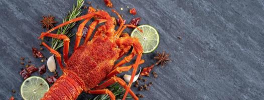 Cooked boiled lobster, delicious dinner seafood meal set with knife and fork on black stone slate background, restaurant menu design, top view, overhead photo