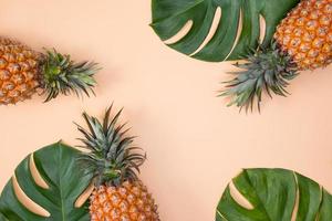 Beautiful pineapple on tropical palm monstera leaves isolated on bright pastel orange pink background, top view, flat lay, overhead above summer fruit. photo