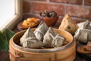 zongzi - bola de masa hervida de arroz chino zongzi en un vapor sobre una mesa de madera con ladrillo rojo, fondo de ventana en casa para el concepto del festival del bote del dragón, de cerca. foto