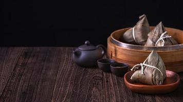 zongzi - bola de masa hervida de arroz chino zongzi en un vapor sobre una mesa de madera fondo retro negro para la celebración del festival del bote del dragón, primer plano, espacio de copia. foto