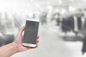 hand holding mobile smart phone with shopping mall blurred background photo