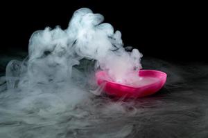 smoke of dry ice with pink heart shaped cup isolated on black background photo