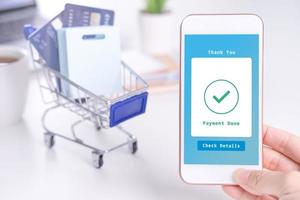 Electronic payment concept, online paying with smart phone, shopping with credit card, laptop over white table background with shop cart trolley, close up. photo