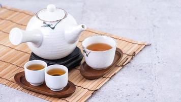 Hot tea in white teapot and cups on a sieve over bright gray cement background, closeup, copy space design concept. photo