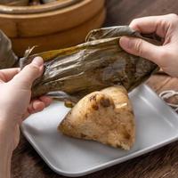 Comer zongzi - bola de arroz del festival del barco del dragón joven mujer asiática comiendo comida tradicional china en una mesa de madera en la celebración de la casa, cerrar foto