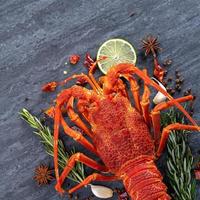 Cooked boiled lobster, delicious dinner seafood meal set with knife and fork on black stone slate background, restaurant menu design, top view, overhead photo