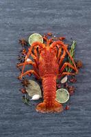 Cooked boiled lobster, delicious dinner seafood meal set with knife and fork on black stone slate background, restaurant menu design, top view, overhead photo