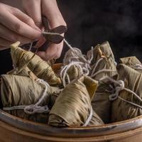 Rice dumpling, zongzi - Bunch of Chinese traditional cooked food on wooden table over black background, concept of Dragon Boat Festival, close up, copy space photo