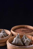 Rice dumpling, zongzi - Dragon Boat Festival, Bunch of Chinese traditional cooked food in steamer on wooden table over black background, close up, copy space photo