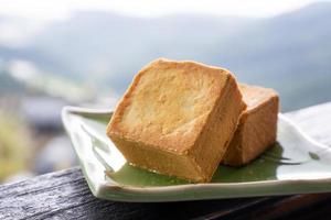 Delicious pineapple pastry in a plate for afternoon tea on wooden railing of a teahouse in Taiwan with beautiful landscape in background, close up. photo