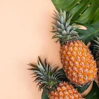 Beautiful pineapple on tropical palm monstera leaves isolated on bright pastel orange yellow background, top view, flat lay, overhead above summer fruit. photo