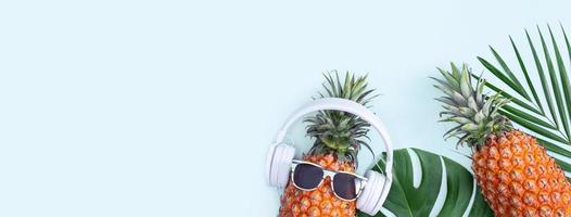 piña divertida con auriculares blancos, concepto de escuchar música, aislada en fondo azul con hojas de palma tropical, vista superior, diseño plano. foto
