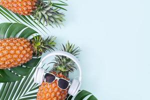 Funny pineapple wearing white headphone, concept of listening music, isolated on blue background with tropical palm leaves, top view, flat lay design. photo