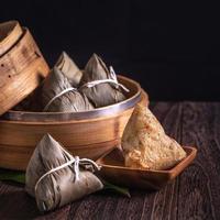 Rice dumpling, zongzi - Dragon Boat Festival, Bunch of Chinese traditional cooked food in steamer on wooden table over black background, close up, copy space photo