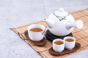 Hot tea in white teapot and cups on a sieve over bright gray cement background, closeup, copy space design concept. photo