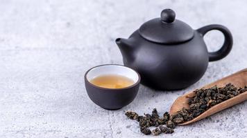 té caliente en tetera negra y tazas y hojas de té secas sobre fondo de cemento gris brillante, primer plano, concepto de diseño de espacio de copia. foto