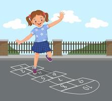 happy little girl playing hopscotch drawn with chalk outside on playground street at the park