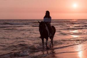 mujer vestida de verano disfruta montando a caballo en una hermosa playa de arena al atardecer. enfoque selectivo foto