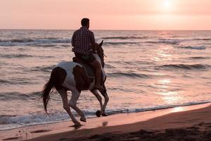 un hombre moderno con ropa de verano disfruta montando a caballo en una hermosa playa de arena al atardecer. enfoque selectivo foto