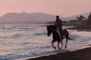 un hombre moderno con ropa de verano disfruta montando a caballo en una hermosa playa de arena al atardecer. enfoque selectivo foto