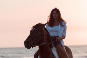 Woman in summer clothes enjoys riding a horse on a beautiful sandy beach at sunset. Selective focus photo