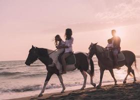 The family spends time with their children while riding horses together on a beautiful sandy beach on sunet. photo