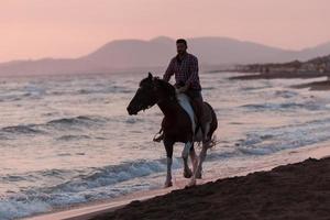 un hombre moderno con ropa de verano disfruta montando a caballo en una hermosa playa de arena al atardecer. enfoque selectivo foto