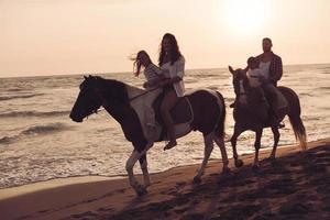 The family spends time with their children while riding horses together on a beautiful sandy beach on sunet. photo