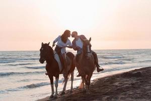 una pareja amorosa vestida de verano montando a caballo en una playa de arena al atardecer. mar y puesta de sol de fondo. enfoque selectivo foto