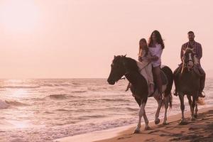 The family spends time with their children while riding horses together on a sandy beach. Selective focus photo