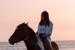 mujer vestida de verano disfruta montando a caballo en una hermosa playa de arena al atardecer. enfoque selectivo foto