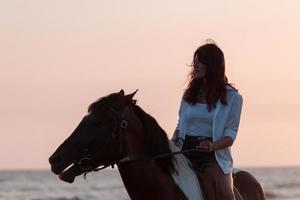 Woman in summer clothes enjoys riding a horse on a beautiful sandy beach at sunset. Selective focus photo