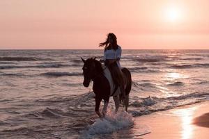 mujer vestida de verano disfruta montando a caballo en una hermosa playa de arena al atardecer. enfoque selectivo foto