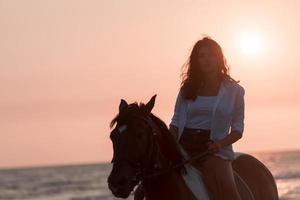 mujer vestida de verano disfruta montando a caballo en una hermosa playa de arena al atardecer. enfoque selectivo foto