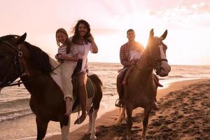 The family spends time with their children while riding horses together on a sandy beach. Selective focus photo