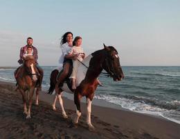 The family spends time with their children while riding horses together on a sandy beach. Selective focus photo