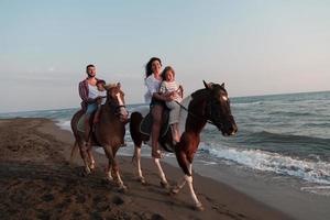 The family spends time with their children while riding horses together on a sandy beach. Selective focus photo