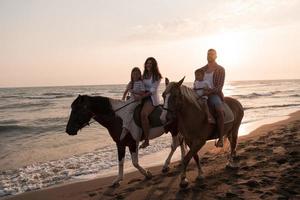 The family spends time with their children while riding horses together on a sandy beach. Selective focus photo