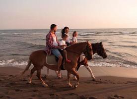 The family spends time with their children while riding horses together on a sandy beach. Selective focus photo