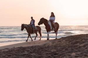 a loving couple in summer clothes riding a horse on a sandy beach at sunset. Sea and sunset in the background. Selective focus photo