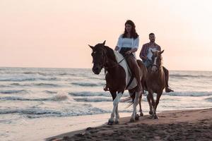 a loving couple in summer clothes riding a horse on a sandy beach at sunset. Sea and sunset in the background. Selective focus photo