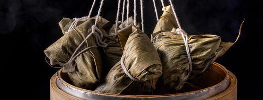 Rice dumpling, zongzi - Bunch of Chinese traditional cooked food on wooden table over black background, concept of Dragon Boat Festival, close up, copy space