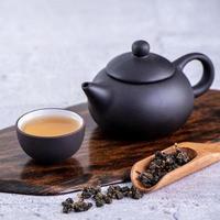 Hot tea in black teapot and cups and dry tea leaves over bright gray cement background, close up, copy space design concept. photo