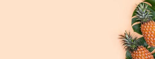 Beautiful pineapple on tropical palm monstera leaves isolated on bright pastel orange pink background, top view, flat lay, overhead above summer fruit. photo