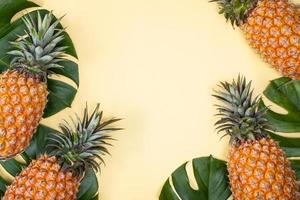 Beautiful pineapple on tropical palm monstera leaves isolated on bright pastel yellow background, top view, flat lay, overhead above summer fruit. photo