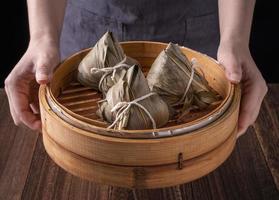 Rice dumpling, zongzi - Bunch of Chinese traditional cooked food on wooden table over black background, concept of Dragon Boat Festival, close up, copy space photo