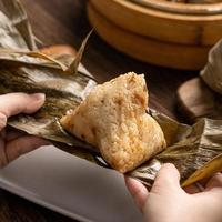 Comer zongzi - bola de arroz del festival del barco del dragón joven mujer asiática comiendo comida tradicional china en una mesa de madera en la celebración de la casa, cerrar foto