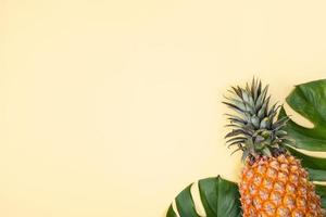 Beautiful pineapple on tropical palm monstera leaves isolated on bright pastel orange yellow background, top view, flat lay, overhead above summer fruit. photo
