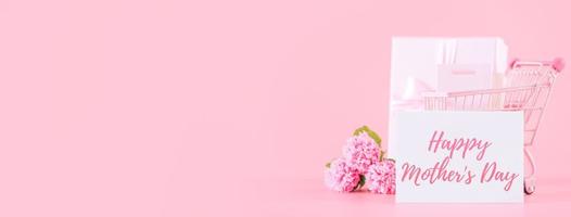 Mother's Day holiday gift design concept, pink carnation flower bouquet with wrapped box isolated on light pink background, copy space. photo