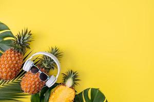 Funny pineapple wearing white headphone, listen music, isolated on yellow background with tropical palm leaves, top view, flat lay design concept. photo